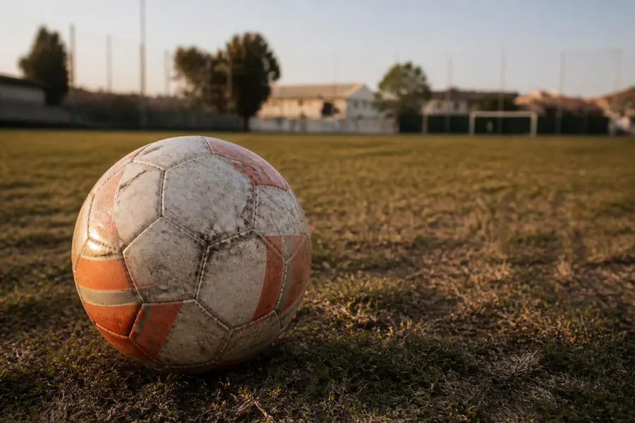 Scuffed football on dry grass of a Spanish municipal pitch