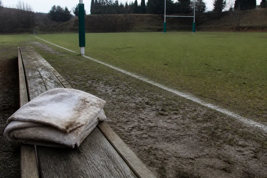 Muddy rugby sideline with a folded towel on a wooden bench